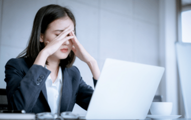 Eine Frau sitzt verzweifelt vor ihrem Laptop und hält sich die Hand an den Kopf 