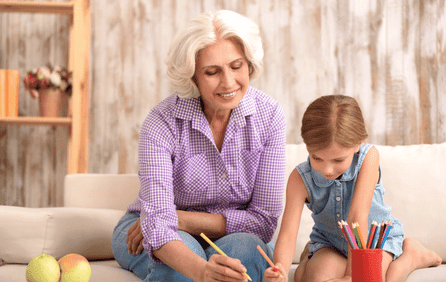 A grandmother and her granddaughter sit on the couch and paint together  